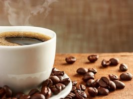 Xícara com café quente e grãos de café na mesa | Efeitos do café na digestão