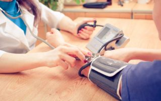 Médica medindo a pressão arterial de paciente | Alimentos que ajudam a regular a pressão