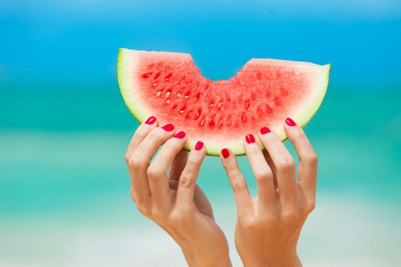 foto de mulher segurando melancia na praia | Alimentação no verão: como desfrutar a estação de forma saudável